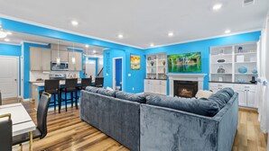 A modern living room with a blue accent wall, a fireplace, and a kitchen area in the background. - Stylish & Central Townhome in the Heart of Raleigh (Raleigh)
