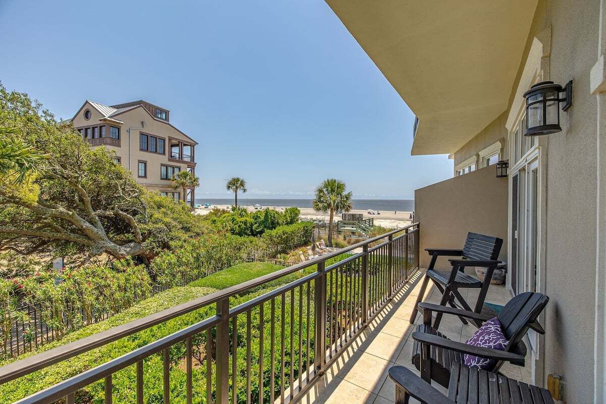 Ein Balkon mit Blick auf den Strand, eine Palme und ein Gebäude im Hintergrund.