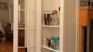 Et hvidt skab med åbne døre, der viser hylder med glas og køkkenudstyr.