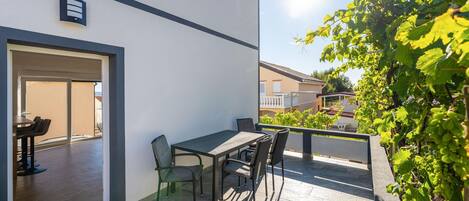 Een terras buiten met een tafel en stoelen, een schuifdeur en uitzicht op een aangrenzend gebouw.