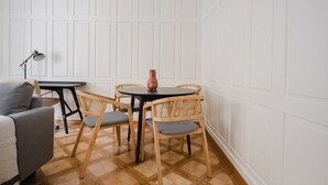 Huoneessa on puulattia, pyöreä pöytä tuoleineen, harmaa sohva ja lattiavalaisin.