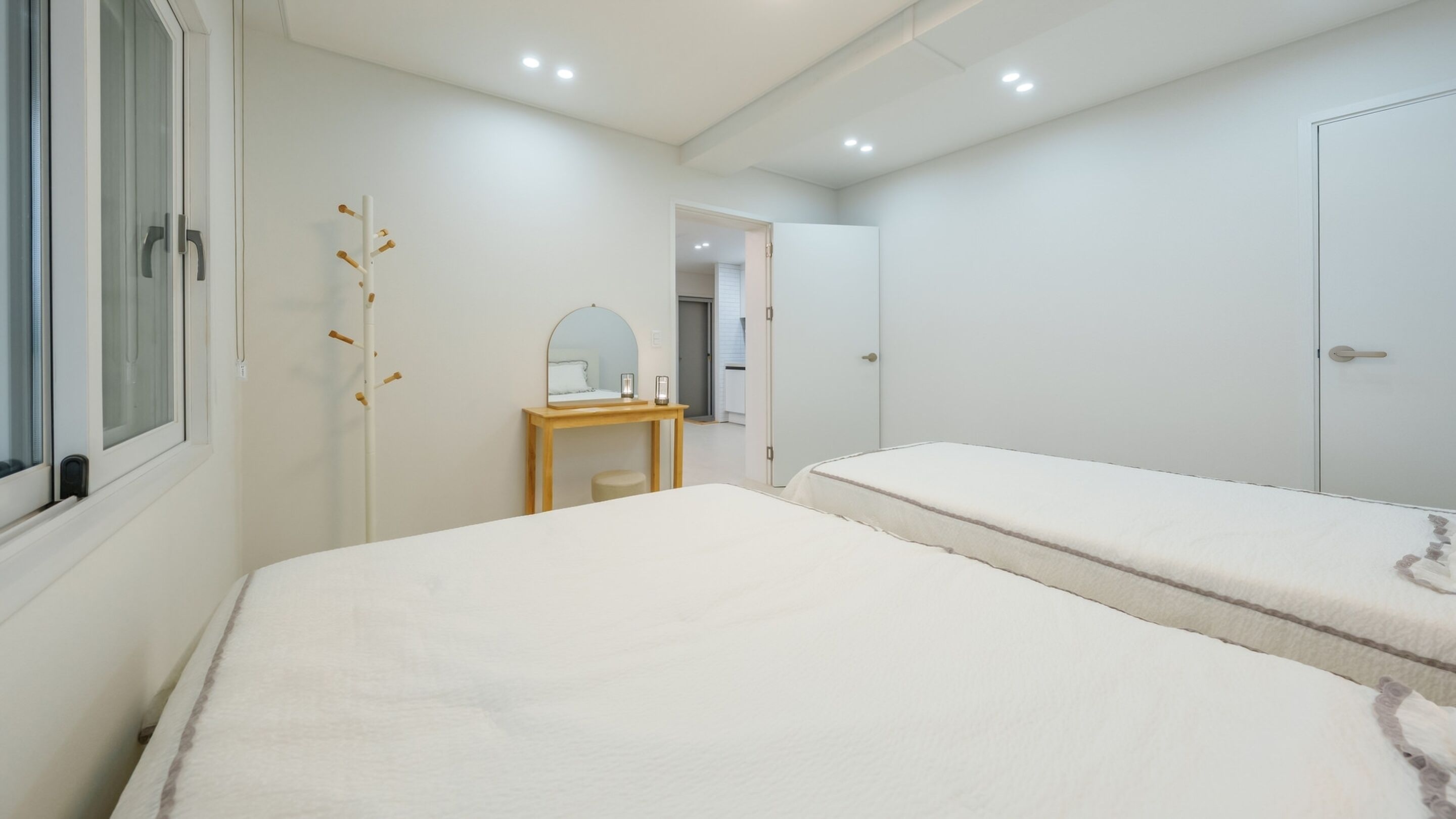Un dormitorio con dos camas, una mesita de noche de madera, un espejo y un perchero.