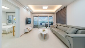 Una habitación de hotel moderna con balcón, una cama, un sofá, un televisor y una pequeña mesa.