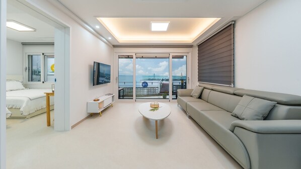 A modern hotel room with a balcony, a bed, a sofa, a TV, and a small table. - Yeosu Eoneumeosjinnal Pension (Yeosu)