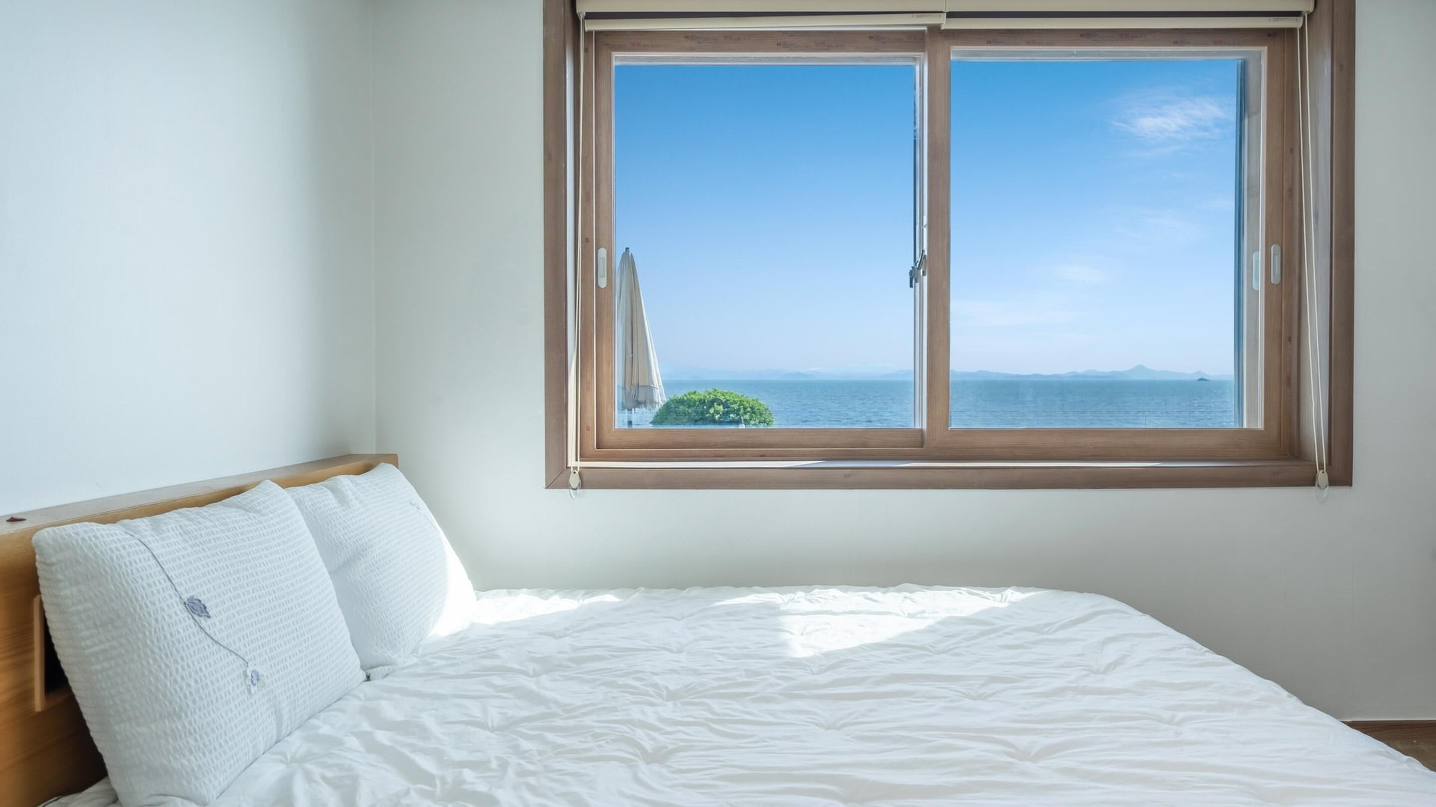 A bedroom with a large window overlooking a body of water and distant land.