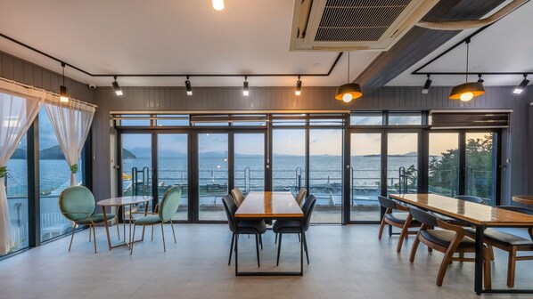 A modern dining area with large windows offering a view of the sea and mountains. - Yeosu Eoneumeosjinnal Pension (Yeosu)