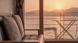 Vue depuis une pièce dont la fenêtre donne sur un plan d’eau et des montagnes, au coucher du soleil.