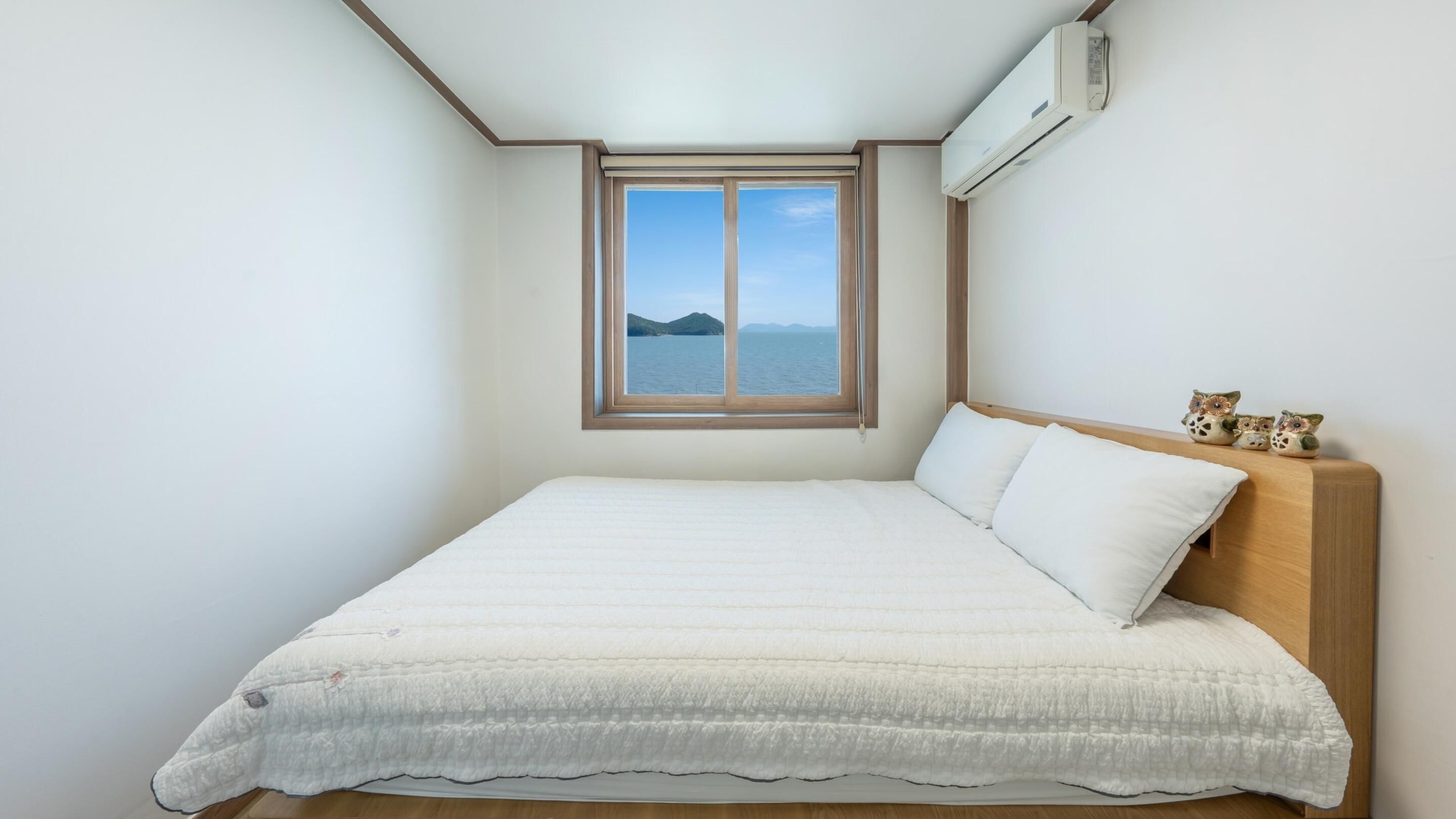 Un dormitorio con una cama grande, una ventana con vista al mar y un equipo de aire acondicionado.