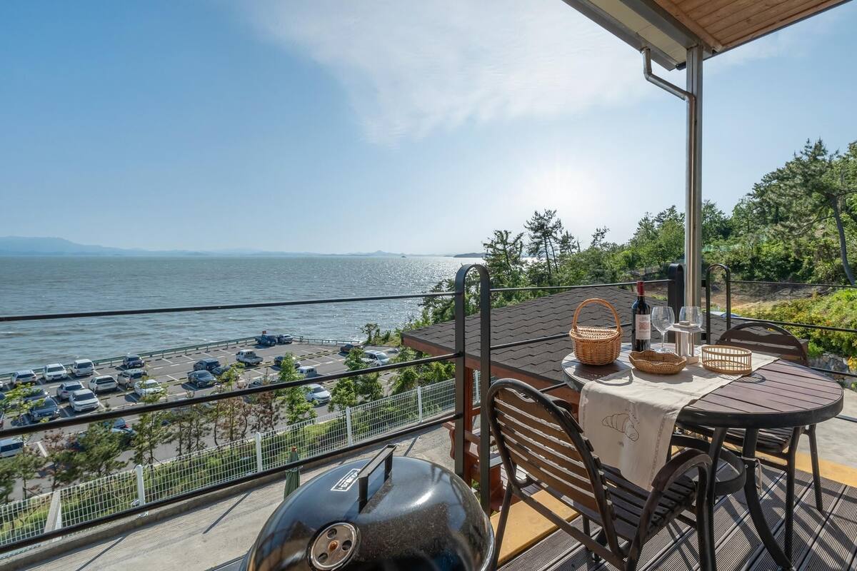 Terraza con mesa lista para comer, con vista a un cuerpo de agua y un estacionamiento.