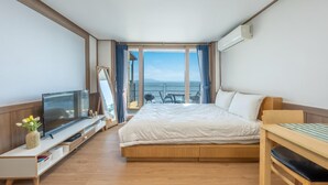 Habitación de hotel con cama, televisión, escritorio de madera y vista al mar.
