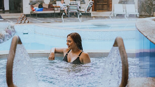 A pool area with a person in the water, lounge chairs, and a stone wall in the background. - QUINTA LOS JUANES (Baños de Agua Santa)