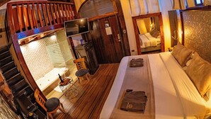 A cozy bedroom with a large bed, a wooden chair, a small table with a bottle, and a television on a wooden stand. - QUINTA LOS JUANES (Baños de Agua Santa)