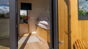 Een moderne slaapkamer met een houten vloer, een bed met witte lakens, een nachtkastje met een vaas bloemen en een aan de muur bevestigde televisie.