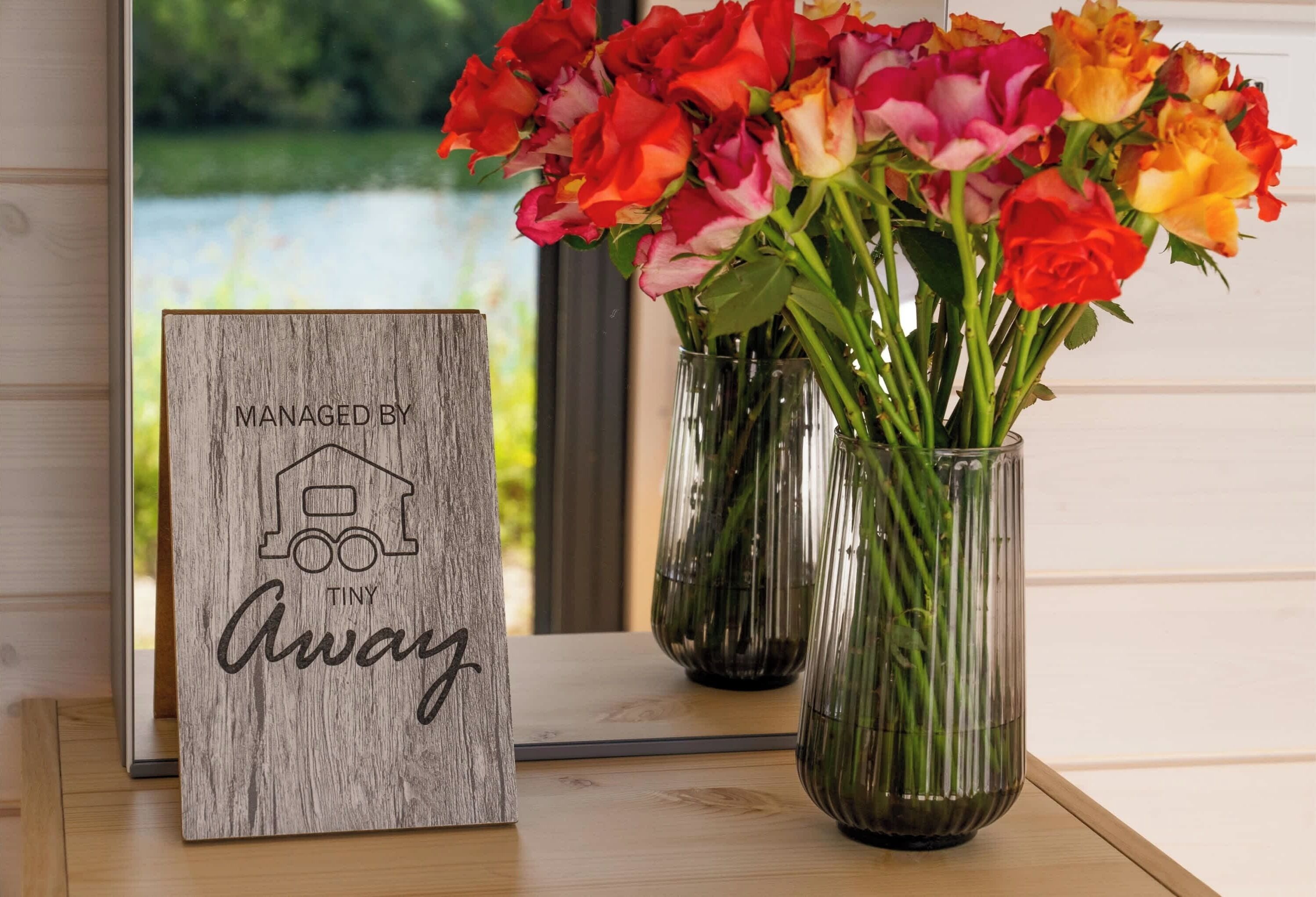 Une enseigne en bois avec du texte et un vase rempli de roses aux couleurs vives.