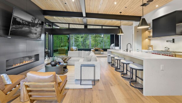 A modern interior with a fireplace, seating area, kitchen, and large windows.