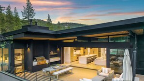 A modern house with a spacious outdoor area, including a dining table and seating, a kitchen, and a large glass door leading to a patio.