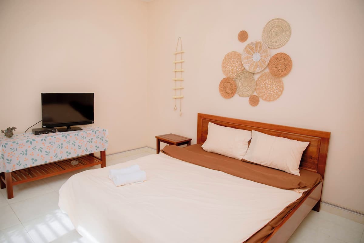 Un dormitorio ordenado con una cama, un televisor sobre una mesita y un adorno en la pared.