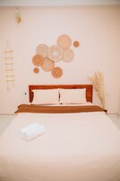 Un dormitorio con una cama de madera, ropa de cama blanca y una pared decorada con piezas de arte tejidas circulares.