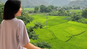 A person overlooking a landscape with green fields and distant mountains during sunset. - Mami Home - Homestay Lac Village (Mai Ha)