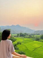 Una persona contempla un paisaje con campos verdes y montañas lejanas al atardecer.