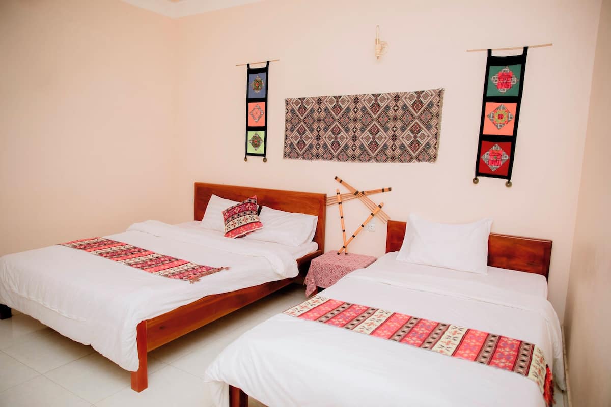 Una habitación con dos camas de madera, cada una con ropa blanca y un plaid estampado. Hay adornos en la pared sobre las camas y una lámpara fijada a la pared.