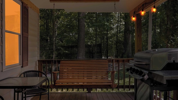 Une véranda avec un banc en bois, un barbecue et une table.