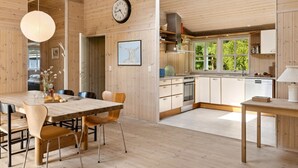 Une pièce spacieuse avec un décor intérieur en bois, un coin repas avec une table et des chaises, une cuisine équipée d’appareils modernes et une lucarne.
