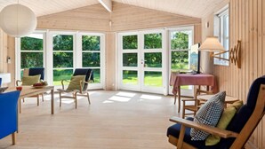 Une pièce spacieuse avec un plancher en bois, de grandes fenêtres et une table avec une lampe.