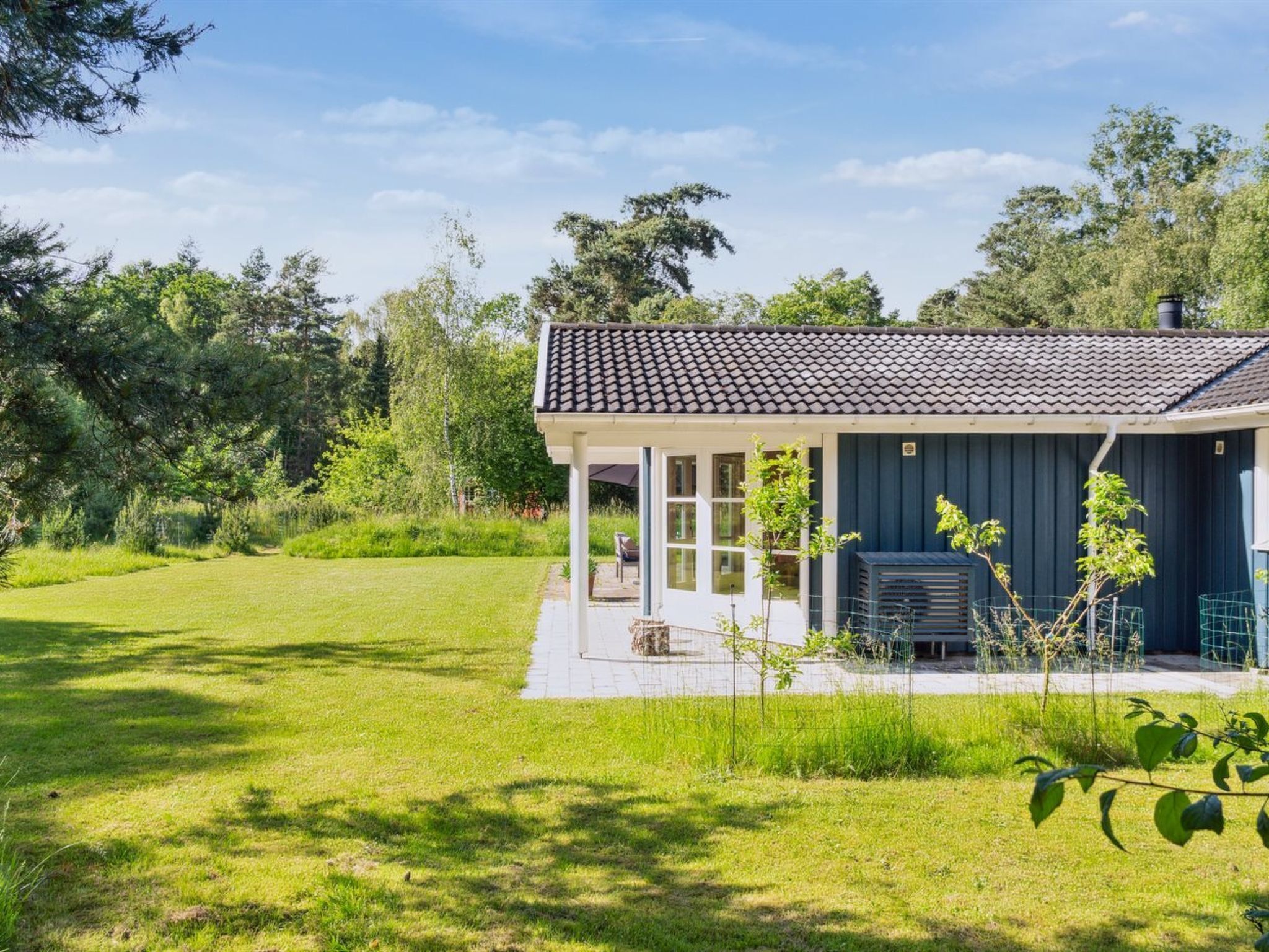 Une maison de plain-pied avec un toit en tuiles, une véranda et un petit jardin.