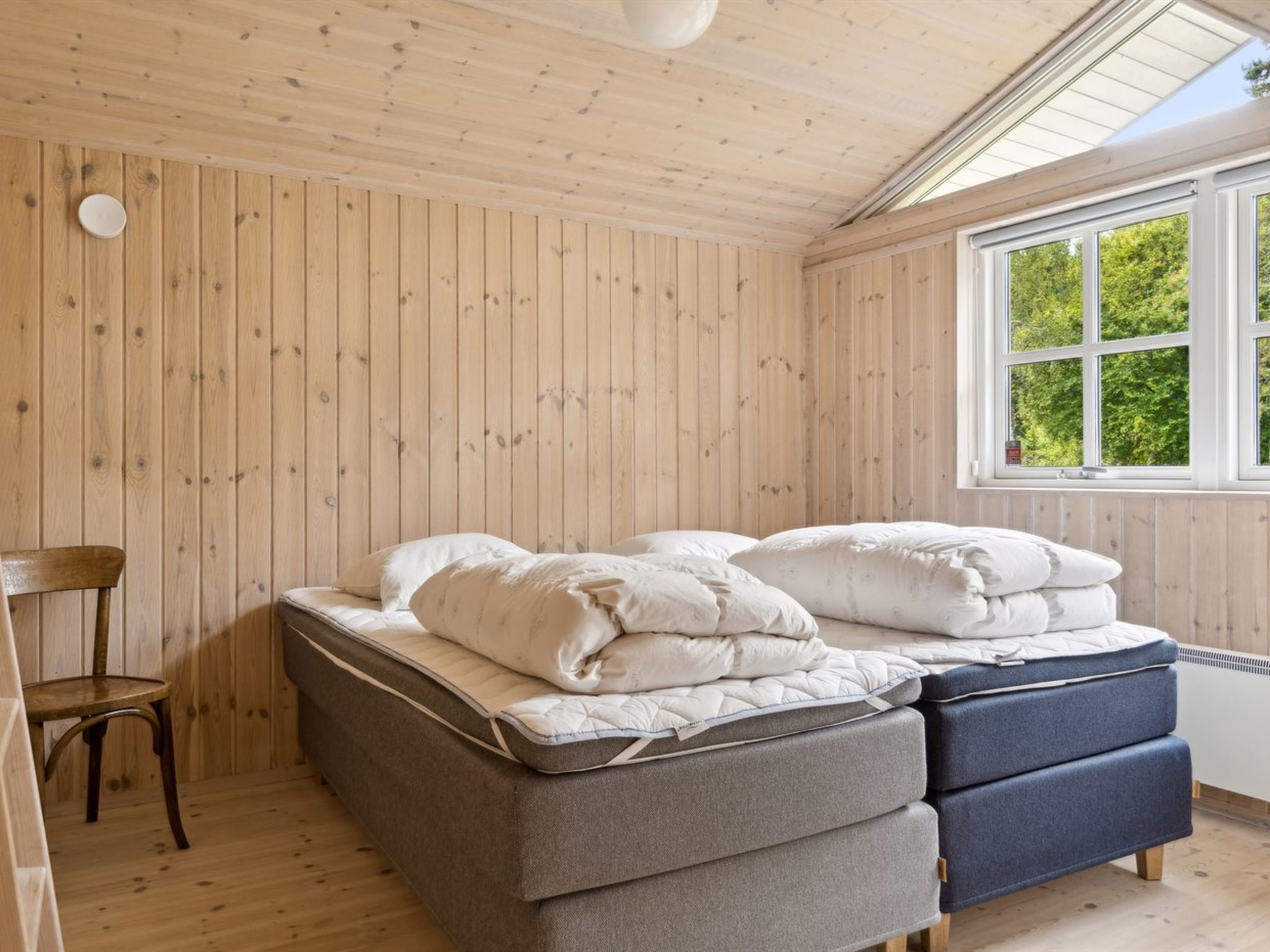 A room with a bed, a chair, and a window with a view of trees.