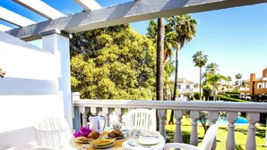Eine Terrasse mit weißem Esstisch und weißen Stühlen, mit Blick auf einen Pool und üppiges Grün.