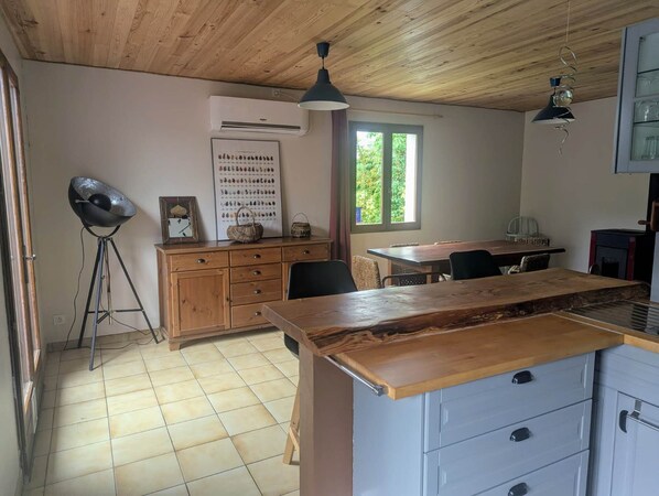 A kitchen with wooden cabinets, a dining table, and a large window. - La Maison D'omélie de Tournemire (TOURNEMIRE)