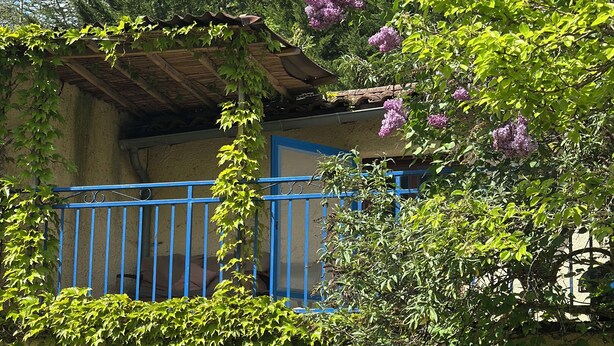 A rustic building with a blue door, a balcony with blue railings, and surrounding greenery. - La Petite Maison D'omélie (TOURNEMIRE)