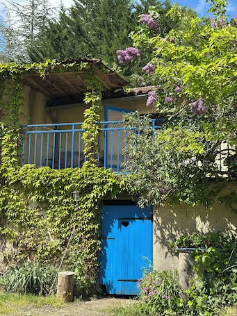 A rustic building with a blue door, a balcony with blue railings, and surrounding greenery.. La Petite Maison D'omélie