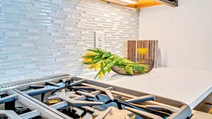 A modern kitchen with a white tiled backsplash, a gas stove, and a power outlet. - Fall in Nashville: 2 homes, rooftop hot tubs, sleeps 24 near downtown (Nashville)