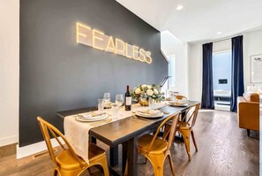 A dining area with a long table set for four, a black wall with a neon sign, and a view of the outdoors through a window. - Nashville getaway: 2 homes, 2 rooftop hot tubs, sleeps 24 near downtown (Nashville)