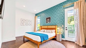 A bedroom with a wooden bed, a blue blanket, a patterned wall, a framed picture, and a window with curtains. - Fall in Nashville: 2 homes, rooftop hot tubs, sleeps 24 near downtown (Nashville)