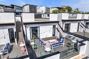 A modern outdoor deck with seating and tables, surrounded by white buildings. - Nashville getaway: 2 homes, 2 rooftop hot tubs, sleeps 24 near downtown (Nashville)