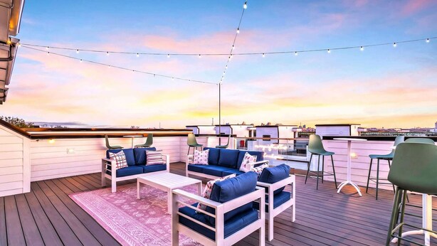 An outdoor deck with blue and white furniture, string lights, and a view of the city skyline at sunset. - Fall in Nashville: 2 homes, rooftop hot tubs, sleeps 24 near downtown (Nashville)