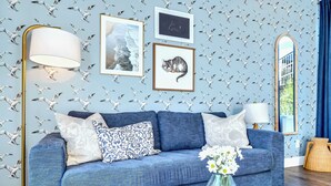 A living room with a blue sofa, a floor lamp, framed pictures, and a mirror. - Fall in Nashville: 2 homes, rooftop hot tubs, sleeps 24 near downtown (Nashville)