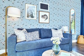 Uma sala de estar com um sofá azul, um abajur, quadros emoldurados e um espelho.
