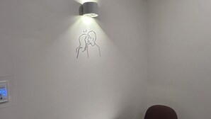 Un mur orné d’un simple dessin linéaire représentant deux personnes qui s’embrassent, un luminaire fixé au mur et un thermostat.
