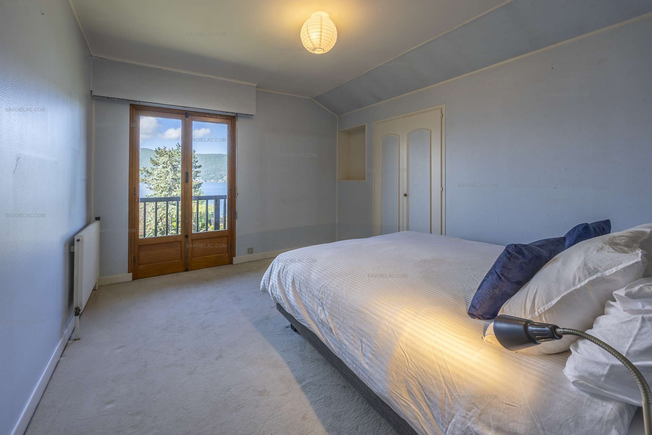 Une chambre à coucher comprenant un lit, une table de chevet, une lampe, un radiateur, une porte et une vue sur l’extérieur.