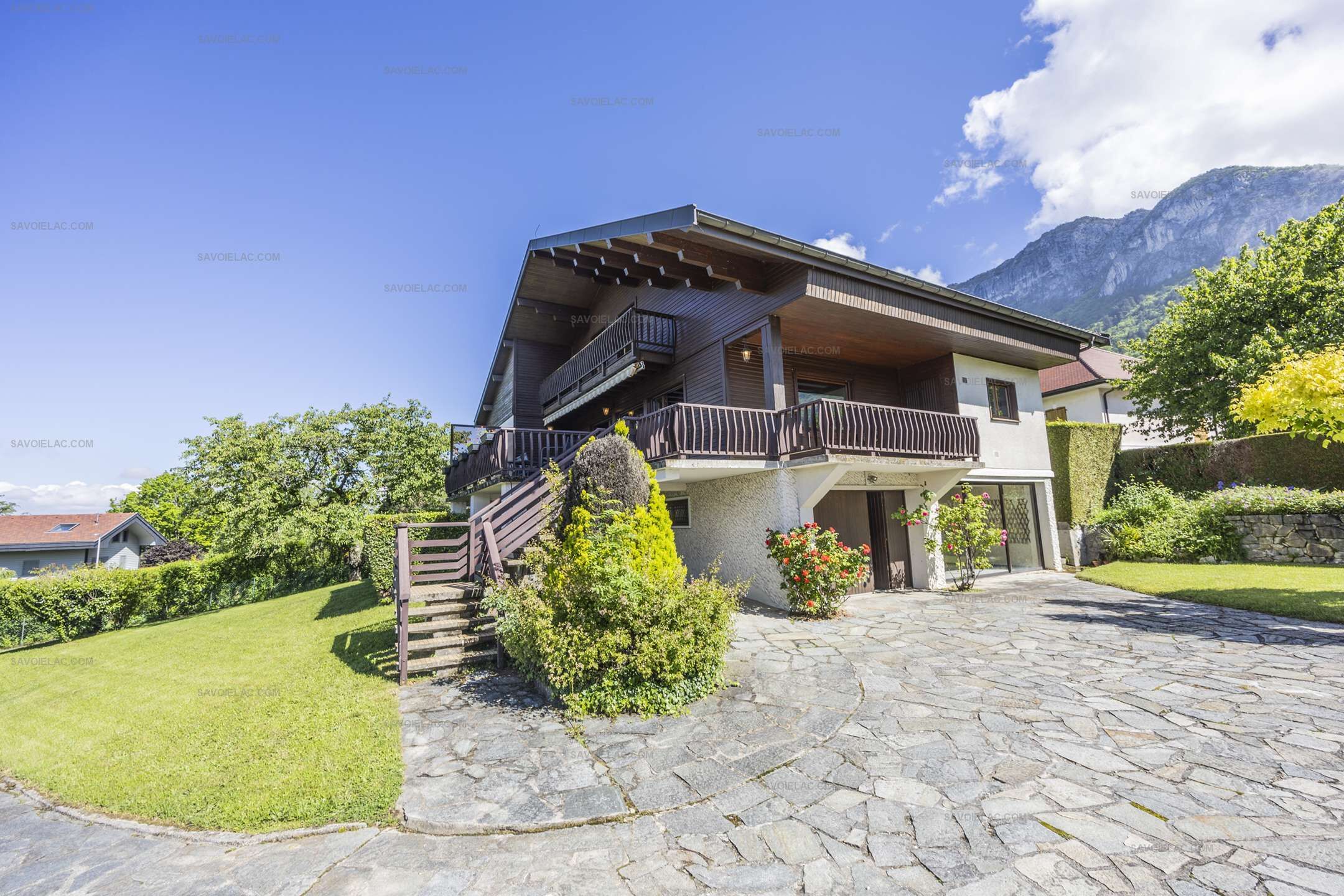 A two-story house with a stone-paved driveway, a wooden staircase, and a balcony.
