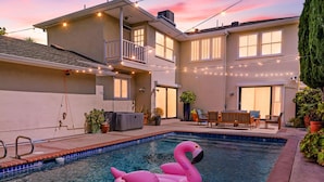 A residential pool with a pink flamingo float, surrounded by a house with a balcony and string lights. - 6BR Villa with Pool, Jacuzzi & Game Room, Walk to Rodeo Drive (Los Angeles)