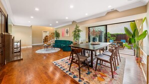 A spacious living area with a wooden dining table, a teal sofa, and a large window offering a view of greenery. - 6BR Villa with Pool, Jacuzzi & Game Room, Walk to Rodeo Drive (Los Angeles)