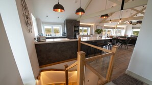 Een moderne keuken met een centraal eiland, een houten trap en hangende lampen.