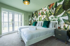Un dormitorio con dos camas, un ventanal con persianas, un mural en la pared y una mesita de noche con lámpara.