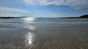 A beach with calm waves, clear skies, and distant landforms. - Bluebells: Eco-Friendly 4-Bed Home with Sea Views in Llanfaelog | Managed by Anglesey Holiday Lettin (Llanfaelog)