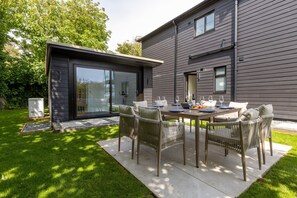 A modern house with a dining area featuring a table and chairs, a sliding glass door, and a well-maintained lawn.